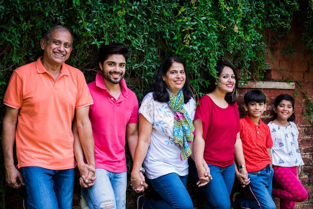 Família indiana em pé na fila contra a parede coberta de trepadeiras. multi geração de família asiática no parque ou jardim se divertindo, conceito de vida familiar saudável