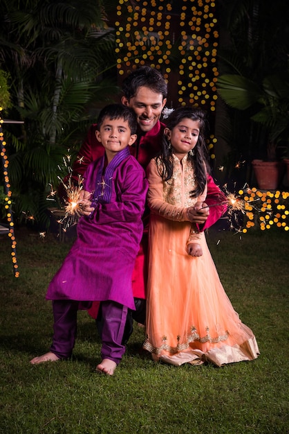 Família indiana em trajes tradicionais brincando com estrelinhas ou phuljhadi enquanto celebra o festival de diwali, ao ar livre