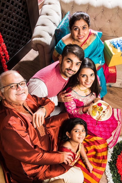 Família indiana feliz comemorando o Festival de Ganesh ou Chaturthi Boas-vindas ou apresentação de Pooja e comendo doces em roupas tradicionais em casa decorada com flores de calêndula