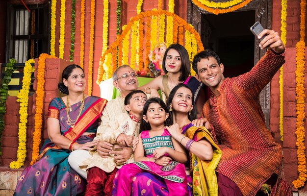 Família indiana feliz comemorando o Festival de Ganesh ou Chaturthi Boas-vindas ou apresentação de Pooja e comendo doces em roupas tradicionais em casa decorada com flores de calêndula