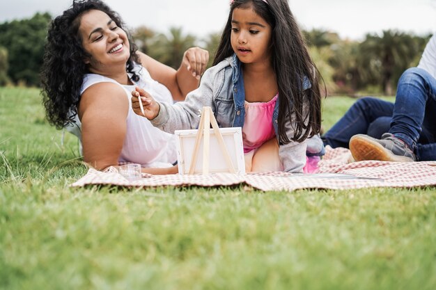 Família indiana feliz se divertindo pintando com crianças ao ar livre no parque da cidade - foco principal no rosto da menina