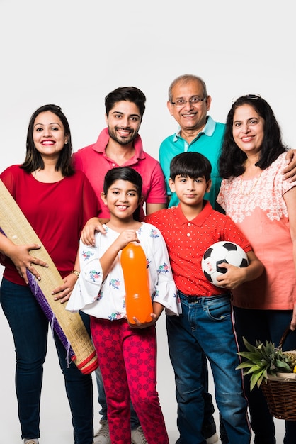 Família indiana indo para o piquenique - multi geração de família asiática em pé sobre um fundo branco com cesta de frutas, tapete, futebol e bebidas. foco seletivo