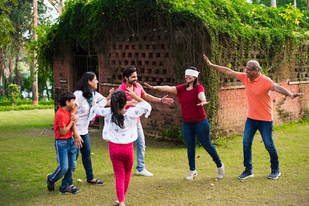 Família indiana jogando com os olhos vendados ou andhali koshimbir no parque ou jardim, família asiática de várias gerações jogando jogos divertidos ao ar livre