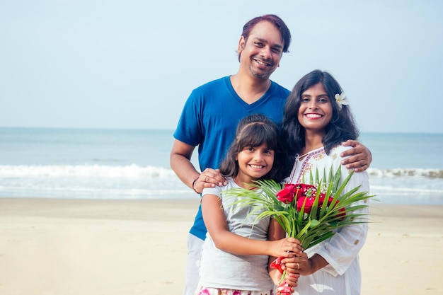 Família indiana jovem relaxando na praia em lindo dia de verão em Goa com buquê de rosas