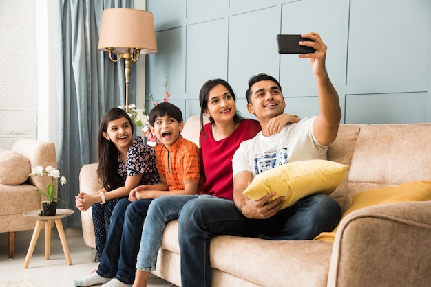 Família indiana sentada no sofá tirando uma foto de selfie usando o smartphone