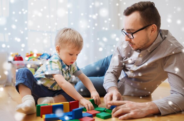 familia, infancia, creatividad, actividad y concepto de personas - padre feliz y hijo pequeño jugando con bloques de juguete en casa sobre la nieve