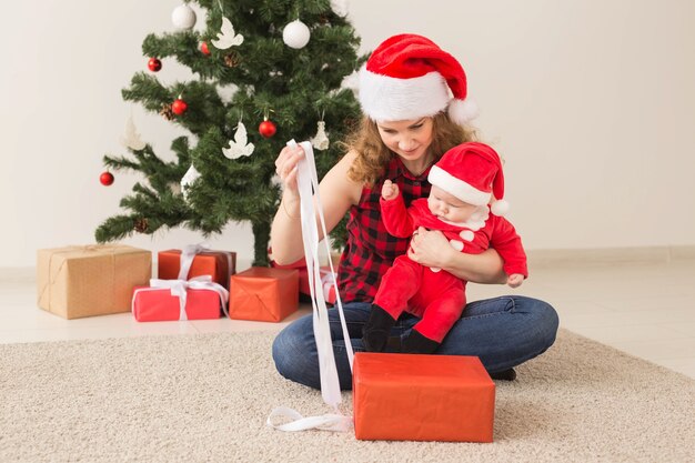 Família, infância e conceito de natal - retrato de mãe feliz e adorável bebê no terno de papai noel.