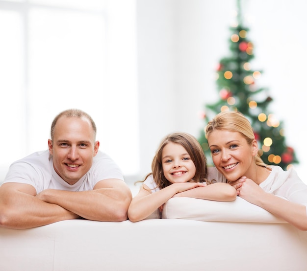 Família, infância, feriados e pessoas - sorrindo mãe, pai e filha sobre a sala de estar e o fundo da árvore de natal