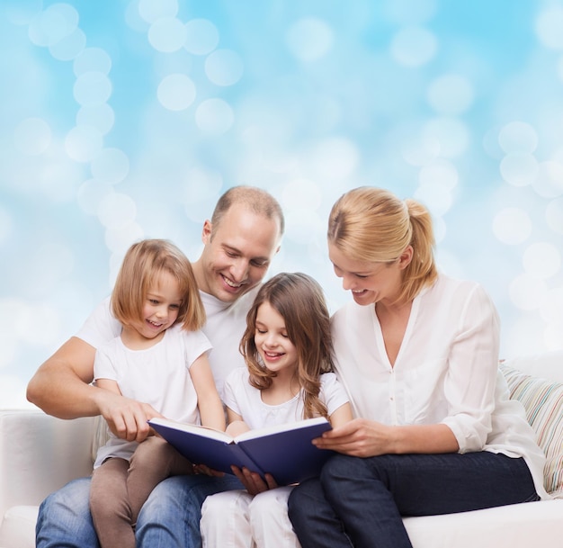 família, infância, feriados e pessoas - sorrindo mãe, pai e meninas lendo livro sobre fundo de luzes azuis