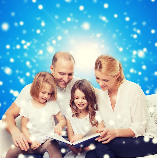 Foto família, infância, férias de natal e pessoas - sorrindo mãe, pai e meninas lendo livro sobre fundo azul nevado