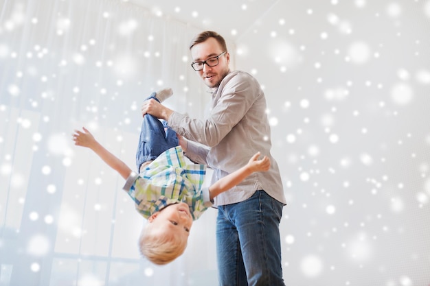 família, infância, paternidade, lazer e conceito de pessoas - pai feliz e filho pequeno brincando e se divertindo em casa sobre a neve