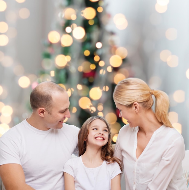 familia, infancia, vacaciones y gente - madre, padre y niña sonrientes sobre el fondo de las luces del árbol de Navidad