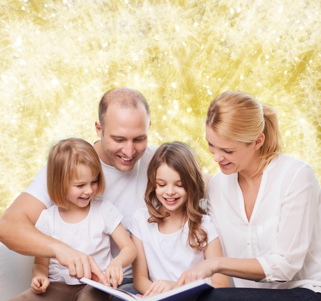 familia, infancia, vacaciones y gente - madre, padre y niñas sonrientes leyendo libros sobre fondo de luces amarillas