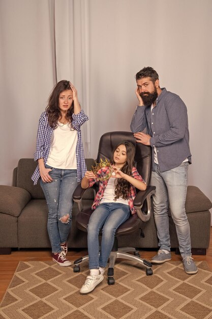 Foto familia infeliz de padre y madre con una niña sosteniendo una corona sentada en una silla en el fracaso del hogar