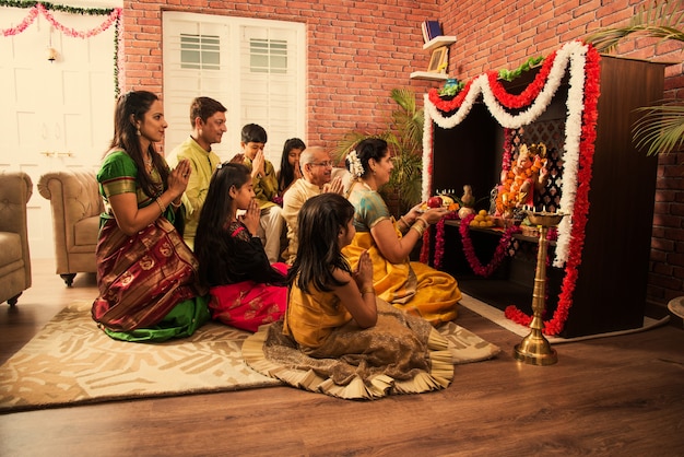 Familia inteligente asiática india realizando Ganesh puja o Aarti en casa mientras usa ropa tradicional