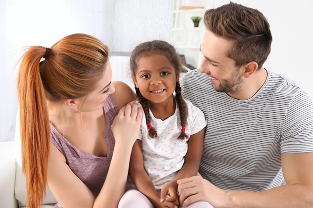 Familia interracial feliz que se sienta en el sofá