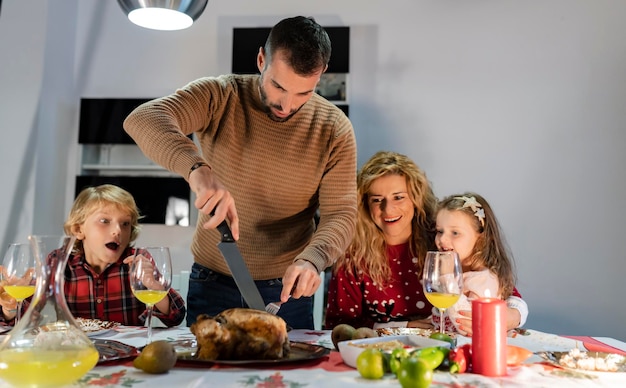 Família jantando de natal em casa, pai esculpe o foco de peru no homem