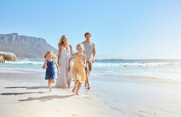 Família jovem alegre com dois filhos correndo na praia e aproveitando as férias de verão Duas garotinhas enérgicas correndo à frente enquanto sua mãe e seu pai seguem em segundo plano