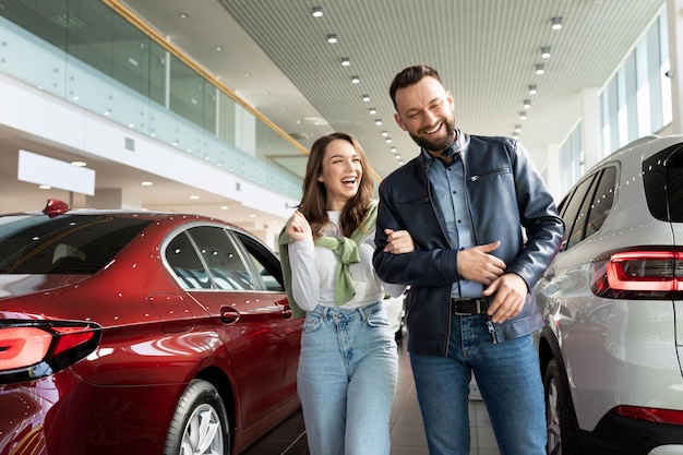 Foto família jovem alegre escolhe entusiasticamente um carro novo em uma concessionária de carros