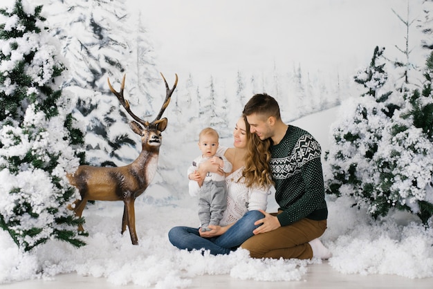 Família jovem amigável: pai, mãe e bebê na floresta de Natal e veados