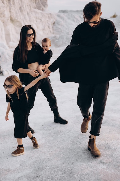 Foto família jovem com 2 filhos vestidos com roupas pretas posando para uma foto durante uma sessão de fotos estilizada em um local branco natural divertido elegante e carismático família com duas filhas