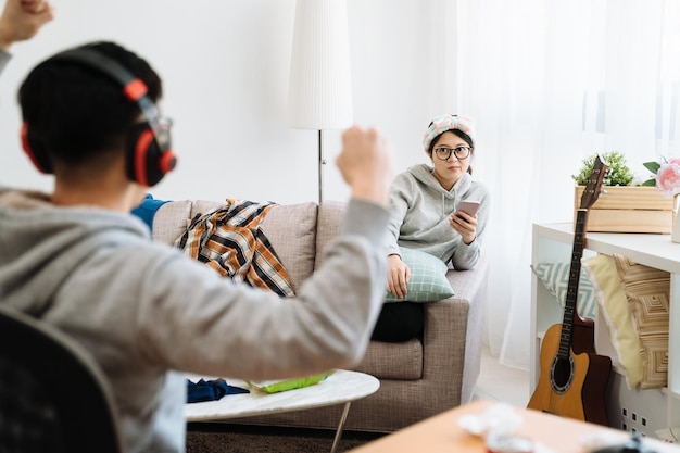 Família jovem com desentendimentos. marido alegre jogando videogame e ganhando compartilhando emoção feliz com a esposa. louca amante fechá-lo enquanto está sentado no sofá usando o celular em uma casa bagunçada.