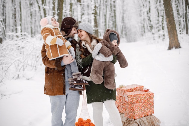 Família jovem com dois filhos em pé na floresta de inverno e posando para uma foto