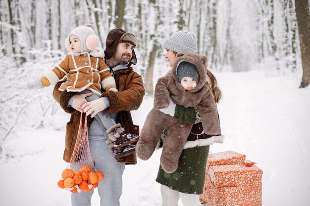 Família jovem com dois filhos em pé na floresta de inverno e posando para uma foto