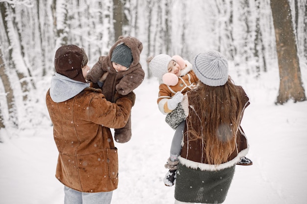 Família jovem com dois filhos em pé na floresta de inverno e posando para uma foto