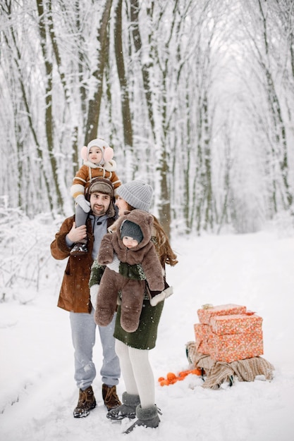 Família jovem com dois filhos em pé na floresta de inverno e posando para uma foto