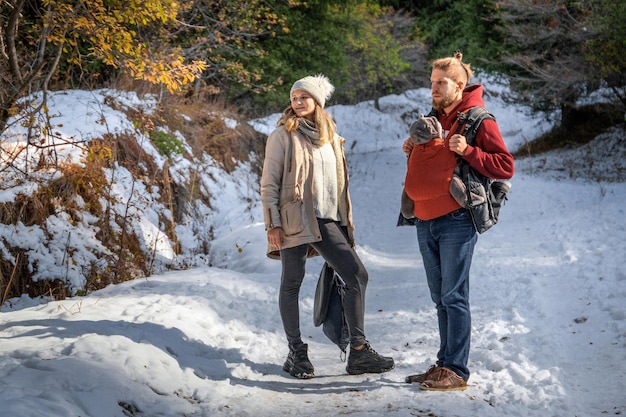 Família jovem com seu bebê no porta-bebês ergonômico na natureza do inverno