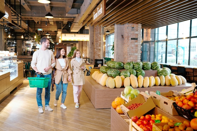 Família jovem e casual de três pessoas se mudando de um grande supermercado contemporâneo enquanto passa por frutas frescas