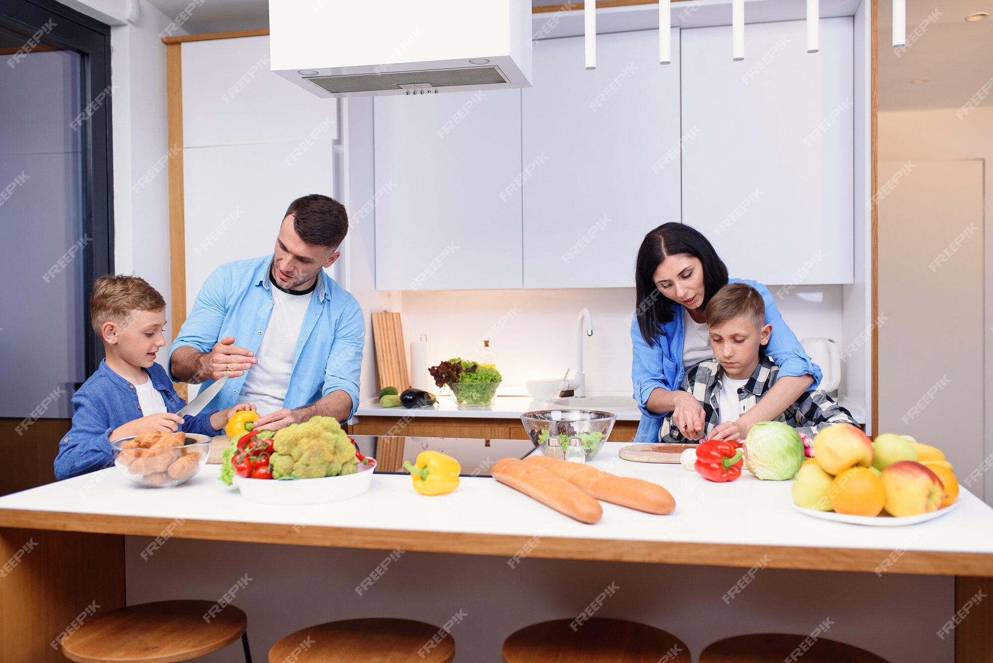 Família jovem e elegante com dois filhos preparando um café da manhã  vegetariano saudável com legumes frescos na cozinha