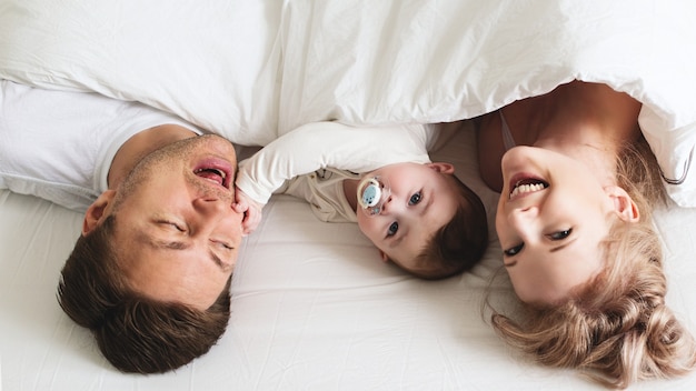 Foto família jovem e engraçada com bebê na cama, estilo de vida de manhã