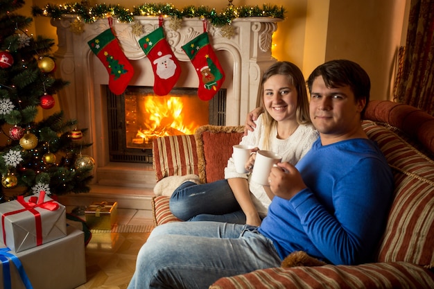 Família jovem e feliz bebendo chá no sofá junto à lareira