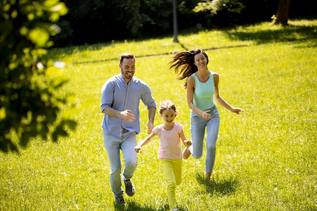 Família jovem e feliz com a filhinha correndo no parque em um dia ensolarado
