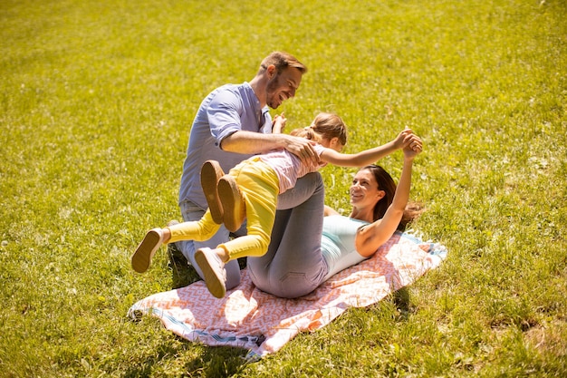 Família jovem e feliz com a filhinha se divertindo no parque em um dia ensolarado