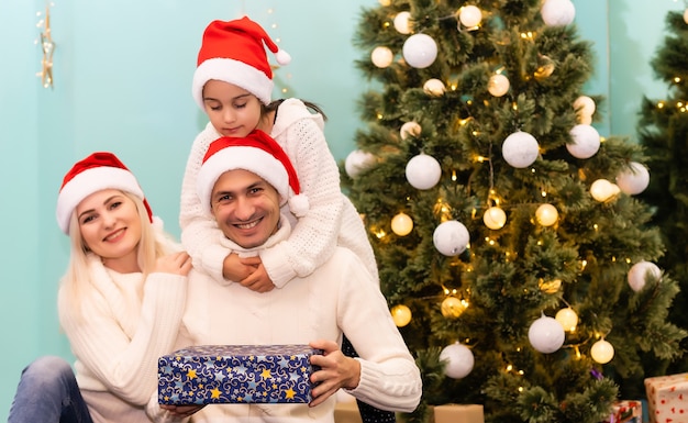 Família jovem e feliz com uma criança segurando um presente de Natal e sorrindo para a câmera