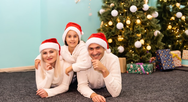 Família jovem e feliz com uma criança segurando um presente de Natal e sorrindo para a câmera