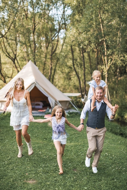 Família jovem em boho casual wear, pai, mãe e duas filhas de mãos dadas e correndo