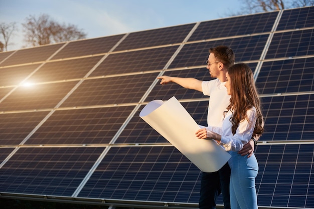 Família jovem está de pé com o plano em suas mãos e observando como os painéis solares estão carregando no local perto de casa