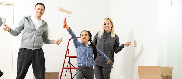 Família jovem feliz com filha pintando a parede.