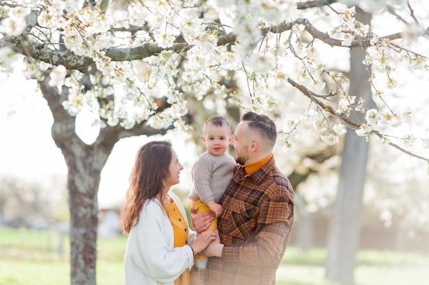 Família jovem feliz com filho pequeno caminha no jardim florescente Mãe e pai com bebê de 1 ano Spring