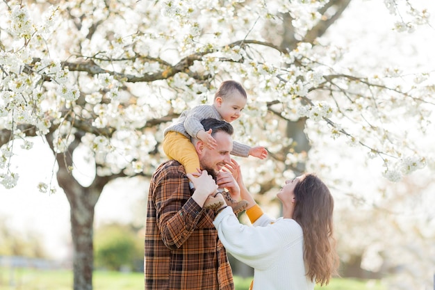 Família jovem feliz com filho pequeno caminha no jardim florescente Mãe e pai com bebê de 1 ano Spring