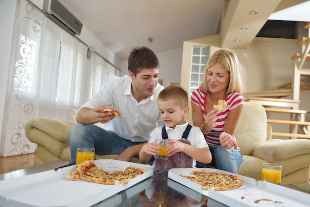 Família jovem feliz comendo pizza saborosa com queijo e suco de laranja fresco e saudável