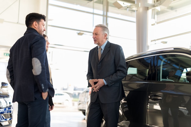 Família jovem feliz conversando com o vendedor e escolhendo seu novo carro em um showroom