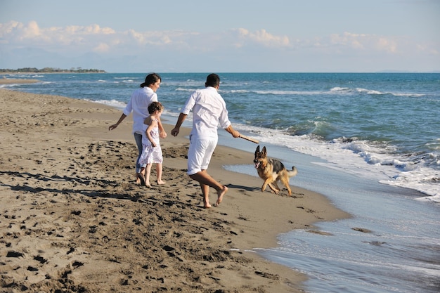 família jovem feliz em roupas brancas se divertir e brincar com lindo cachorro de férias na bela praia