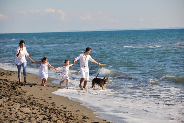 família jovem feliz em roupas brancas se divertir e brincar com lindo cachorro de férias na bela praia