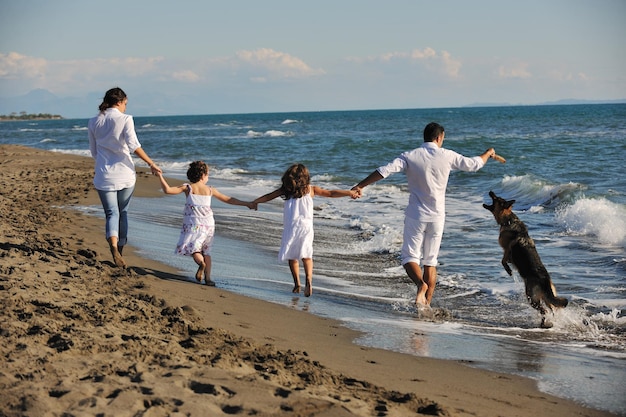 família jovem feliz em roupas brancas se divertir e brincar com lindo cachorro de férias na bela praia