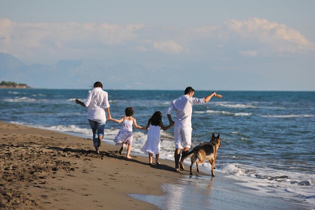 família jovem feliz em roupas brancas se divertir e brincar com lindo cachorro de férias na bela praia